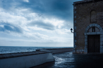 Dark moody alley seen in the evening in the spanish town of Sitges, with gloomy cloudy grey sky....