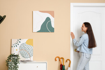 Young woman near door and stylish paintings at home