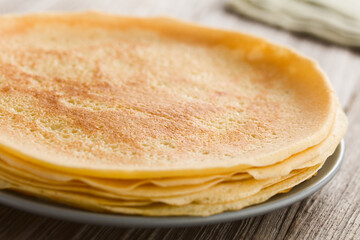 Stack of fresh homemade crepes, thin French-style pancakes, on plate with flour and eggs in the...