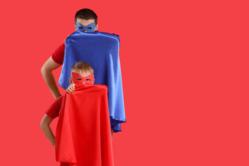Fototapeta premium Little boy with his father in superhero costumes on red background