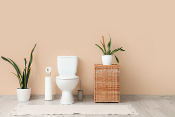 Interior of restroom with toilet bowl, basket and plants near beige wall