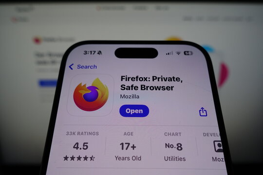 Kiel, SH, Germany March 27 2025: Firefox browser app by Mozilla visible on smartphone screen with company's website displayed on a monitor in the background