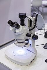 Professional laboratory microscope with dual eyepieces and digital camera attachment, illuminating...