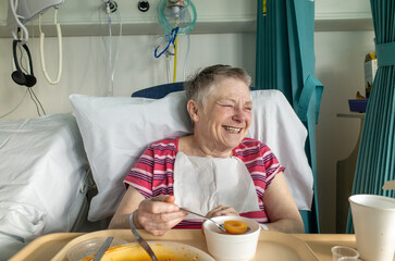 Happy older woman patient laughing in her hospital bed, England, UK