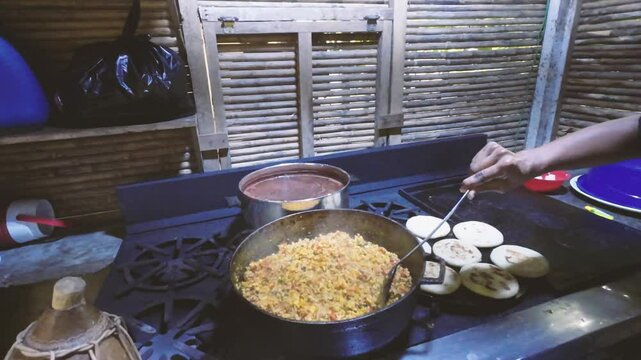 Latin woman cook arepas in budare, perico eggs and hot chocolate for traditional Venezuelan and Colombian breakfast food. Rural kitchen, Venezuela