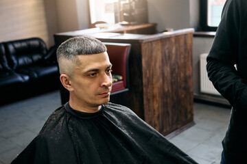 A hairdresser performs a precise haircut on a focused client seated in a contemporary barbershop....