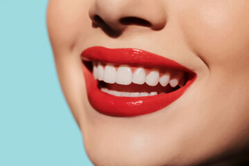 Obraz premium Radiant Close-Up of Smiling Woman with Glossy Red Lips Against Soft Blue Background