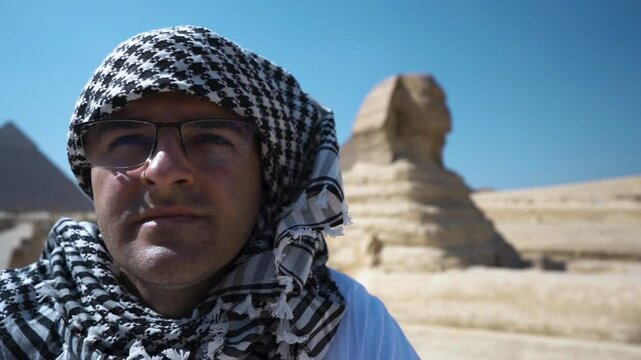 Portrait of a Bedouin man in glasses looking into the distance at the horizon, a sphinx in the background. An Egyptian man contemplates what is happening in the distance