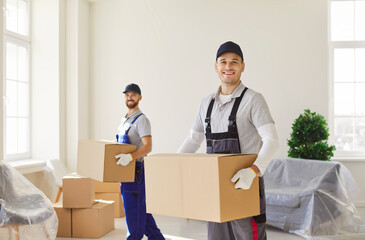 Portrait of smiling professional movers in uniform carrying cardboard boxes and looking at camera....