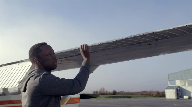 Male Black Pilot Performs Preflight Checks on Wing of Propeller Plane