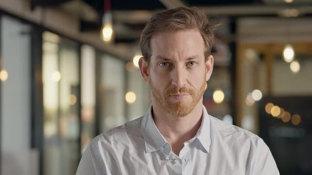White Caucasian man with blue eyes staring directly into camera with strong intense gaze, and confidence. Portrait of businessman with mysterious and intrigue look standing in modern office with bokeh