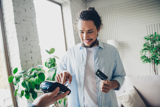 Young man using a credit card and point-of-sale terminal in a modern home interior environment - Powered by Adobe