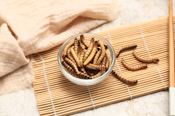 Glass bowl with fried maggots on white background
