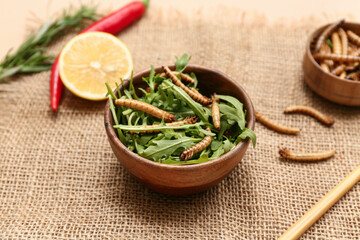 Wooden bowls with fried maggots and arugula on beige background
