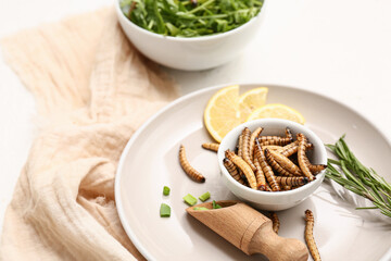 Bowl with fried maggots and slices of lemon on white background
