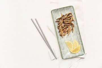 Plate with fried maggots and slices of lemon on white background