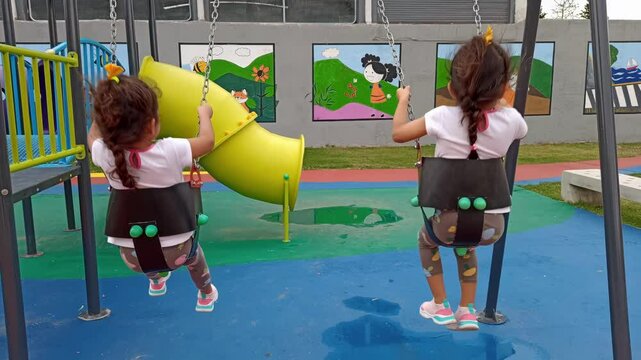 Twin girls playing with swing chairs in park