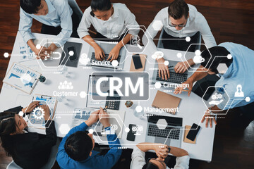 A top-down view of a business team working together on CRM system development, surrounded by digital interfaces and analytical tools in a modern office setting. Amity