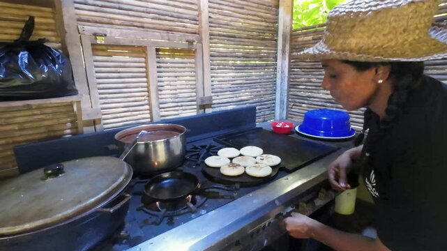 Rustic setting with wooden slat walls. Hispanic woman cooking arepas on Budare, Venezuela