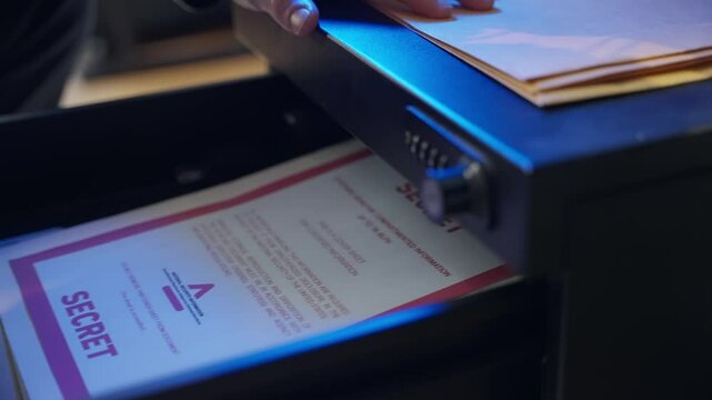 Person stealing classified file folder from office drawer at night. Man taking manila envelope with red label marked as secret for sensitive confidential material and information. Spy agent or a thief