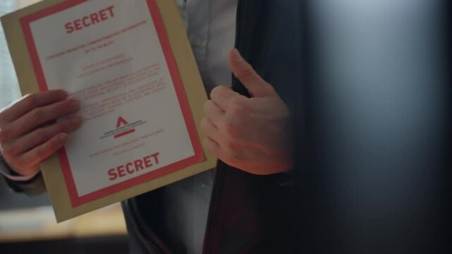 Man discreetly hides secret folder inside his leather jacket in office. Espionage or covert operations. Classified material stolen by agent or spy or mole. Envelope containing intelligence info