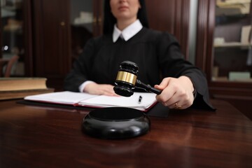 Judge striking gavel at wooden table in office, closeup