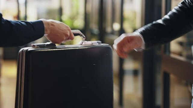 Suited man hands over a suitcase to another, secrecy and suspicion. Government conspiracy or corporate fraud and political corruption.Handshake finalizes transaction. Power and deception collusion