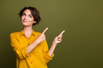 Happy young businesswoman in a yellow blouse pointing with fingers on an elegant green background...
