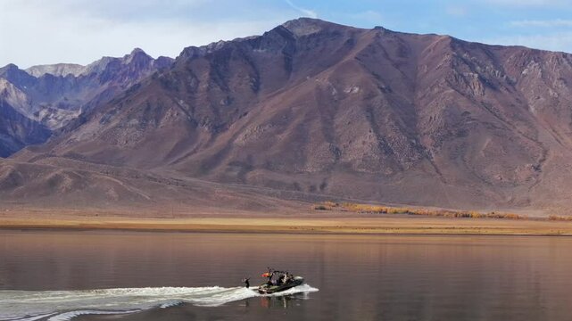 Wake surf surfing water sports MB boat wave Lake Crowley Mammoth Mountain Lakes California aerial drone golden still calm water morning sunny autumn fall family activity follow pan right motion