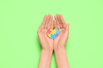 Female hands holding colorful puzzle pieces in shape of heart on green background. Autistic disorder concept