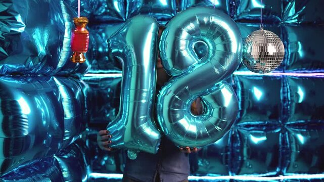 A young woman holds large blue foil balloons shaped as the number 18, marking a special anniversary in a glowing party scene.