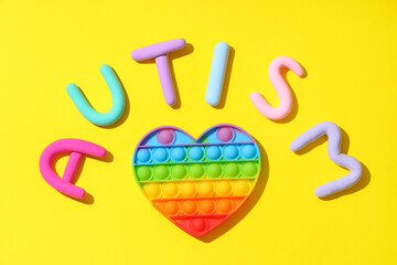 Pop it fidget toy and word AUTISM made from plasticine on yellow background