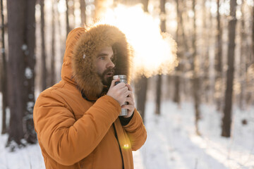 Man warming up with thermos drink in snowy winter forest. Comfort and morning mindfulness in cold...