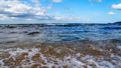 砂浜に打ち寄せる泡立つ波と雲の織りなす景色