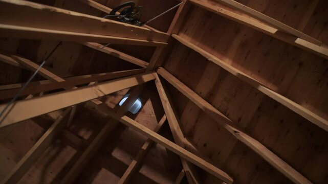 Unfinished attic ceiling with visible wooden framework and a glowing lightbulb.
