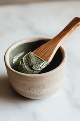 Green clay face mask in a ceramic bowl with a wooden spoon.