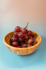Bunch of red grapes in a wooden bowl on a blue background.