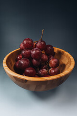 Bunch of red grapes in a wooden bowl on a gray background.