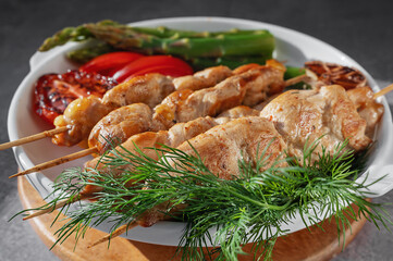 Grilled chicken kebabs with fresh vegetables and herbs on a white plate. Grilled kebabs.