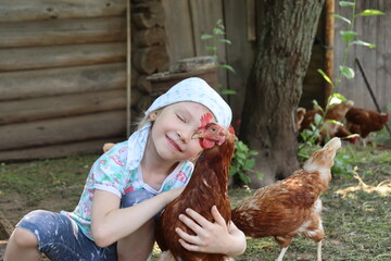 little girl is hugging a brown hen. summer in the village