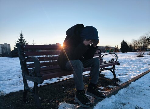 Profile of a sad man complaining sitting on a bench alone in a winter town. lonely guy in the winter park is depressed. Teenage boy alone in the park in the evening.