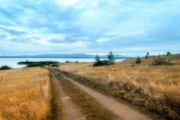 Fototapeta premium Summer cloudy landscape of the Irtyash lake, a lane leading to the lake and mountain range of the Ural mountains at the horizon in Southern Urals in Russia, soft filter applied