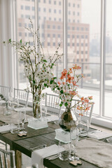 Elegant dining setup with floral centerpieces in modern venue showcasing urban skyline view during daylight