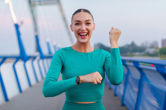 Excited lady celebrating new fitness goal after cardio workout and running training outdoors, looking at camera and shaking fist