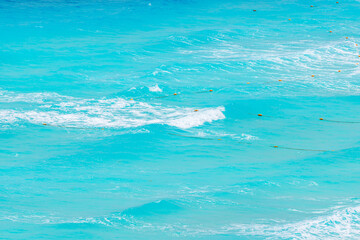 Obraz premium Waves of turquoise Caribbean Sea with floating orange buoys in clear shallow water near beach. Mexico.