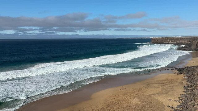 View from above the cliff on the beach below, with massive strong sea, foamy waves, in a sunny day. Amazing strength of nature. Horizontal video. Escalera Beach, Fuerteventura.