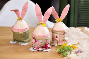 three handmade Easter bunnies made of eggs with pink ears stand on a table against a green wall