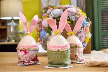 three handmade Easter bunnies made of eggs with pink ears stand on a table against a green wall