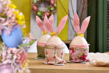 three handmade Easter bunnies made of eggs with pink ears stand on a table against a green wall