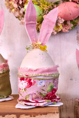 handmade Easter bunnies made of eggs with pink ears and wearing pink pants stands on a table against a green wall